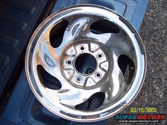 Chrome alloy wheel with five lug holes and a Ford logo stamped in the center