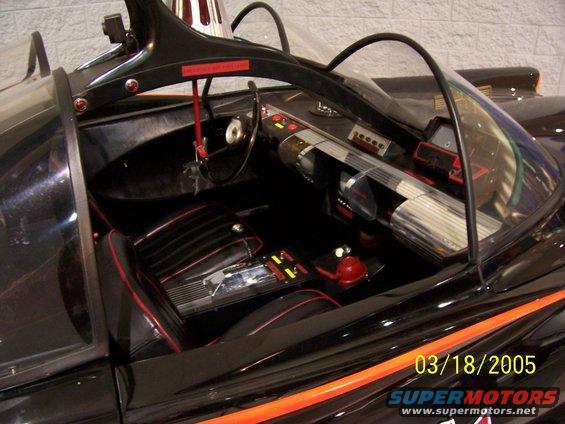 Interior of a black car with red trim, a steering wheel, dashboard controls, and seats