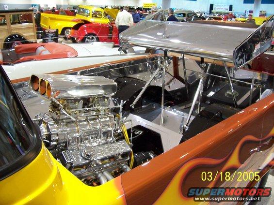 Custom hot rod engine bay with chrome supercharger, orange and yellow flame paint, and a large rear spoiler