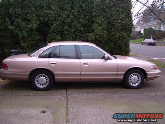 Rose gold sedan parked on a driveway, side view. The car has four doors and a chrome trim line along the bottom of the doors
