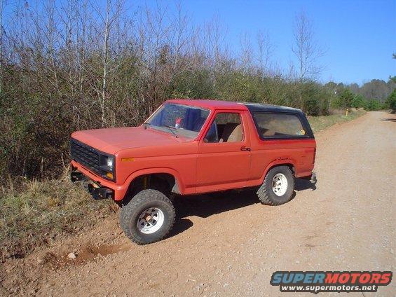 Red Ford Bronco parked on a dirt road with trees in the background