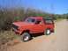 1981 Ford Bronco - This red Ford Bronco is parked on a dirt road, surrounded by trees under a clear blue sky.