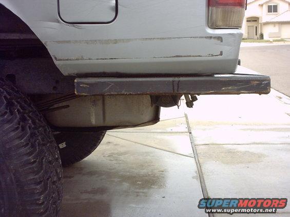 Silver SUV rear bumper, tire, and fuel tank visible. Bumper is scratched and rusty