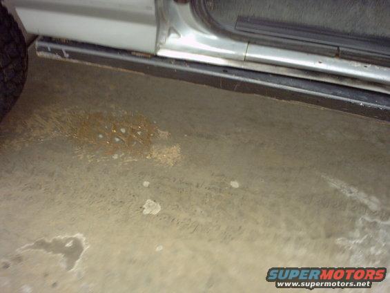 side of a vehicle showing the door, running board, and tire on a concrete floor with some stains