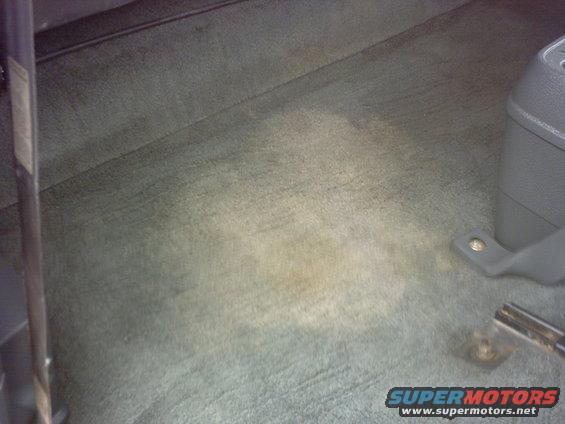 Interior carpet with stains and a gray plastic console piece