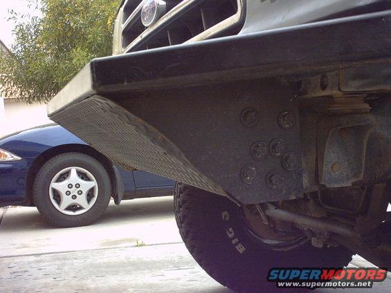 Close-up of a truck's front bumper and tire, with a blue car in the background