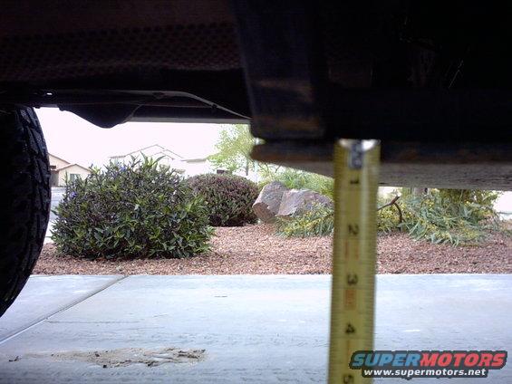 Underside of vehicle frame with tape measure showing ground clearance. Tire visible on left