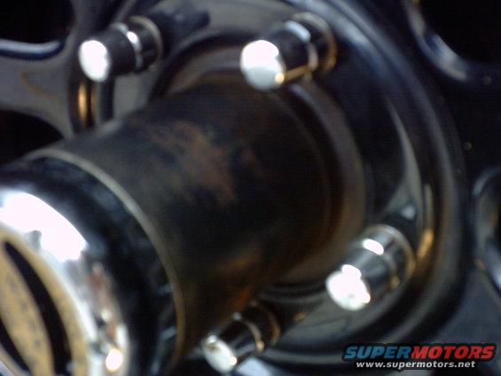 Close-up of a black wheel hub with chrome lug nuts and a silver trim ring