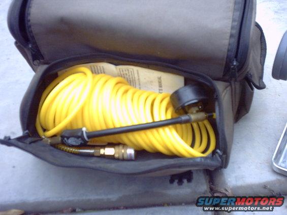 Yellow air compressor hose and gauge inside a black storage bag. A manual is visible underneath the hose