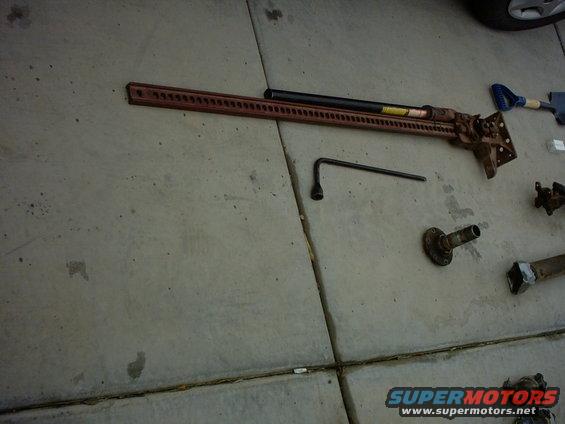 Red hi-lift jack and lug wrench on concrete, with other vehicle parts scattered nearby