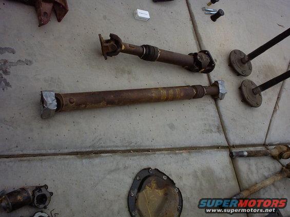 Two rusty driveshafts and differential parts on concrete