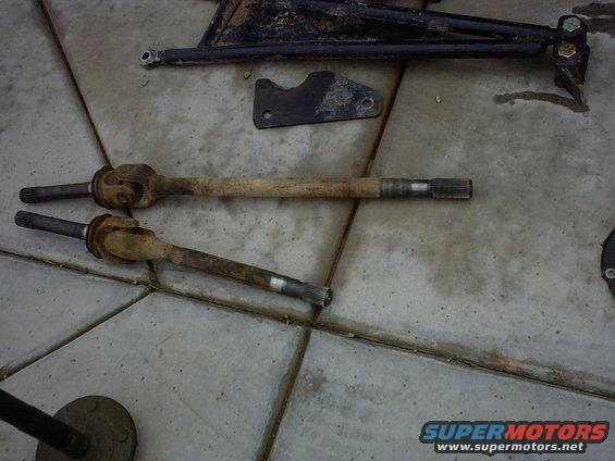 Two rusty drive shafts and black metal suspension components on a tiled floor