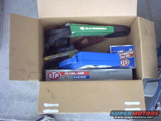 Cardboard box containing car parts: a green Kelly-Springfield belt, an STP oil filter, and a blue oil filter box