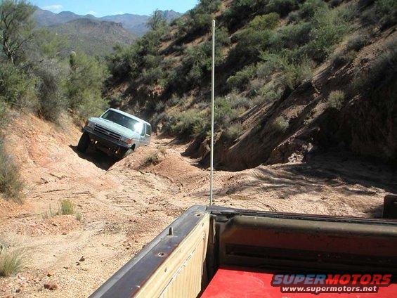 Ford Bronco climbing a dirt hill off-road. Shot from the bed of another vehicle