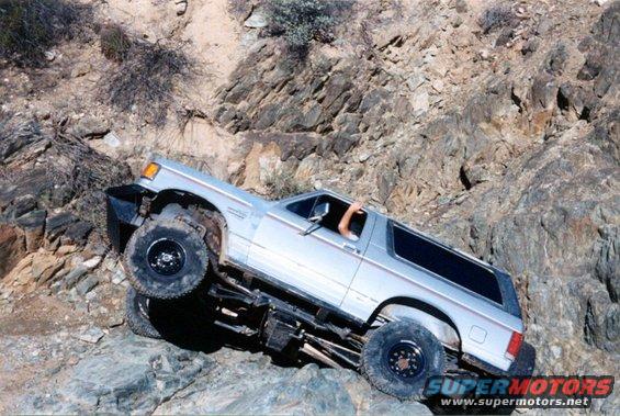 Silver SUV with lifted suspension navigating a steep, rocky incline. Driver's arm is visible outside the window