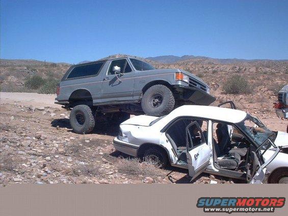 Gray 1990 Ford Bronco lifted over a white sedan