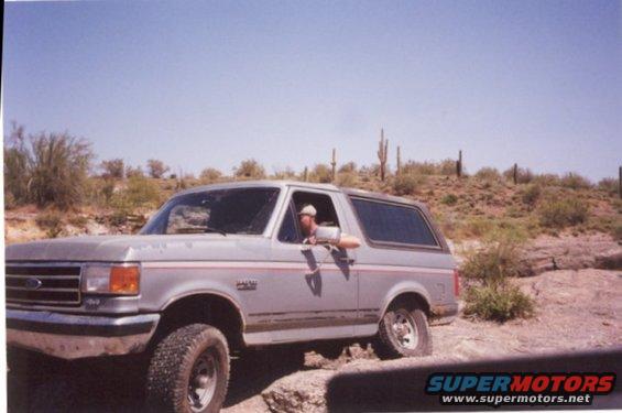 Silver Ford Bronco parked on rocky desert terrain, driver's window down