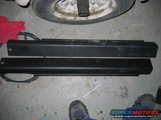 Two black plastic car door trim pieces laid on a concrete floor next to a tire