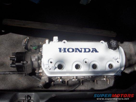 White Honda valve cover with blue lettering, attached to engine components