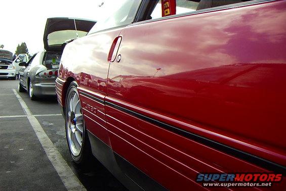 side view of red coupe with black trim and silver wheels, other cars parked behind it