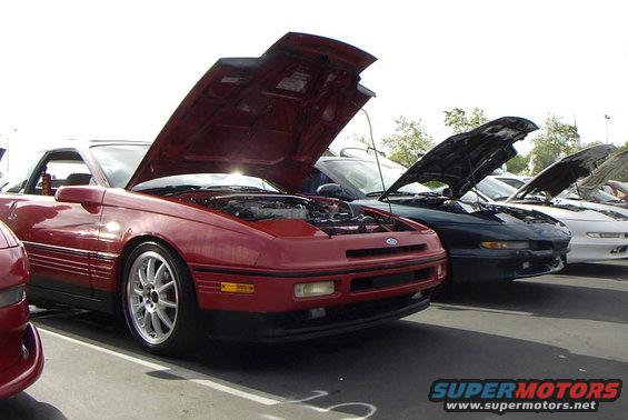 Red 1989 Ford Probe with hood open, parked in a line of cars