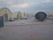 1988 Ford Bronco - A line of quonset huts is visible with several vehicles parked in front, under a cloudy sky.