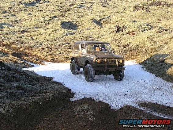 Brown 1970s Ford Bronco driving on snowy terrain