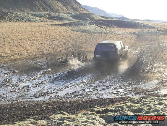 SUV kicking up mud while driving on a dirt track in a barren landscape