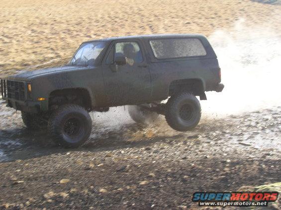 Dark green SUV with lifted suspension and large tires driving off-road, kicking up mud