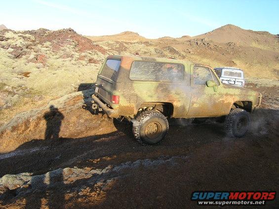 Camouflaged SUV driving on rocky terrain, another SUV in background
