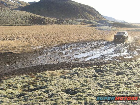 2001 Jeep TJ driving through a muddy track in a barren landscape