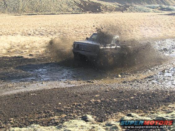 Pickup truck kicking up a huge splash of mud while driving through a muddy track in a barren landscape