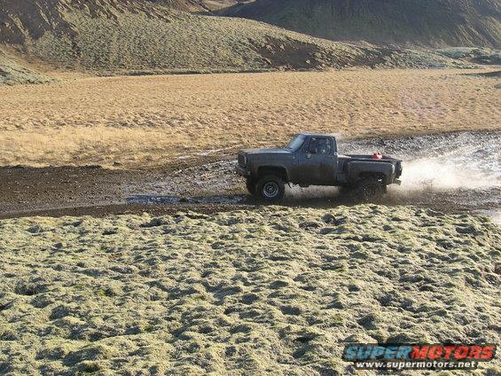 Gray pickup truck driving through water on a dirt road, splashing water