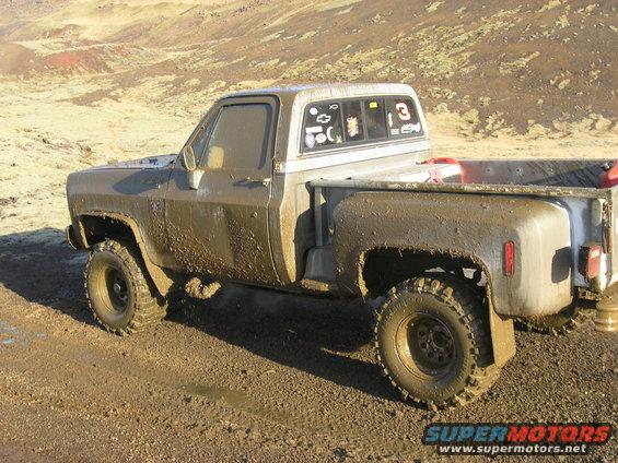 Muddy pickup truck with stickers on the rear window, parked on a dirt road