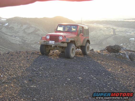 Red Jeep Wrangler parked on a rocky hill with a mountainous background