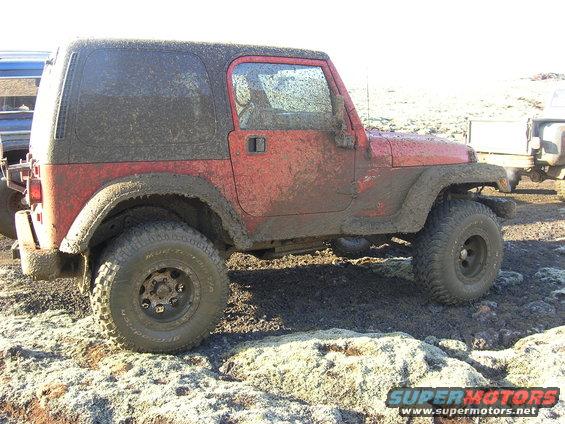 Red 2001 Jeep TJ covered in mud, seen from the side