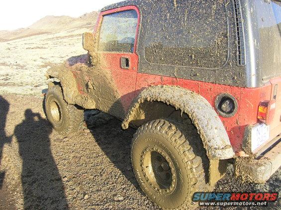Mud-covered red 2001 Jeep TJ parked on a dirt road with mountains in the background
