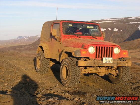 Red 2001 Jeep TJ covered in mud, parked on a dirt road with mountains in the background
