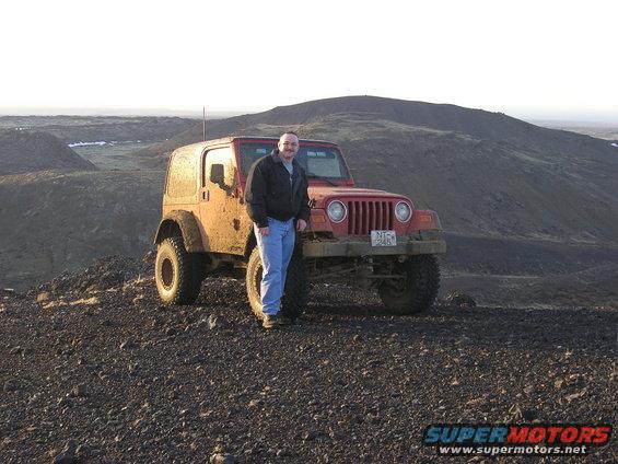 Man standing next to a red 2001 Jeep TJ on a rocky, barren landscape