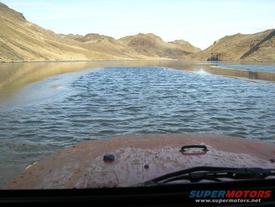 Red Jeep TJ driving through shallow water with mountains in background