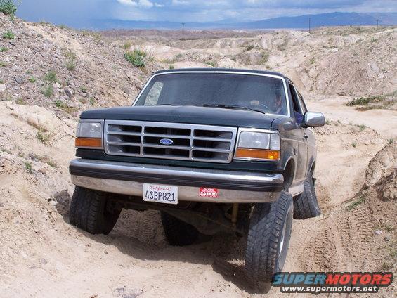 1993 Ford Bronco driving on a dirt trail with large tires