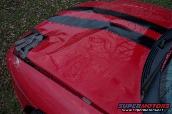 Red car hood with black racing stripes and visible damage near the front left