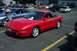 1993 Ford Probe - A red 1993 Ford Probe is parked in a lot, with other vehicles and a building in the background.