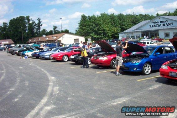 Red sports car with hood up, parked in a lot with other vehicles
