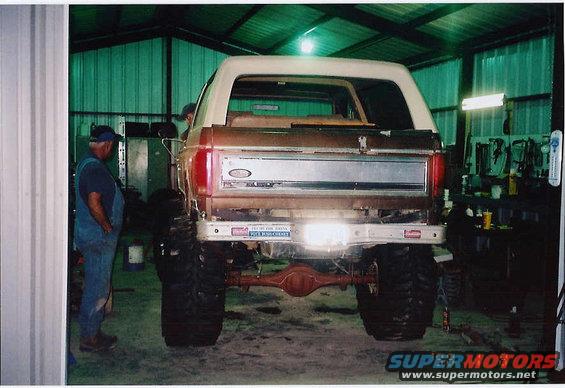 Brown and white Ford Bronco with large tires, viewed from rear in garage