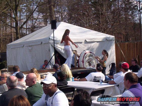Outdoor event with a tent, stage, and audience watching a woman on stage