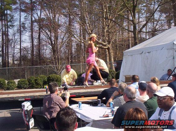 Woman in pink dress on stage, crowd watching, tent in background
