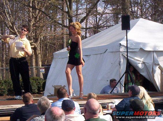 Woman in black dress on stage with a man holding a microphone, audience watching