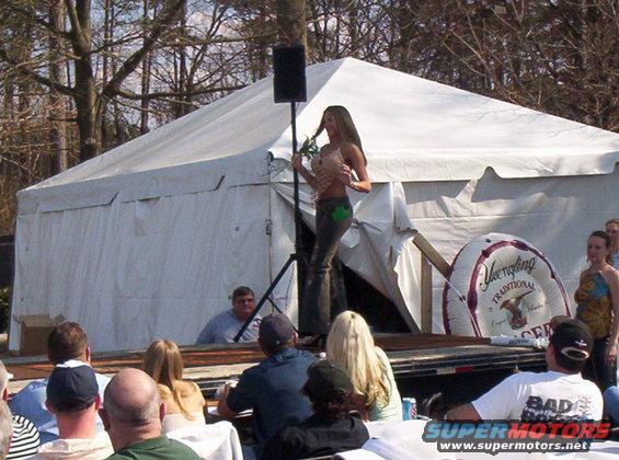 Woman on stage at outdoor event with tent and audience