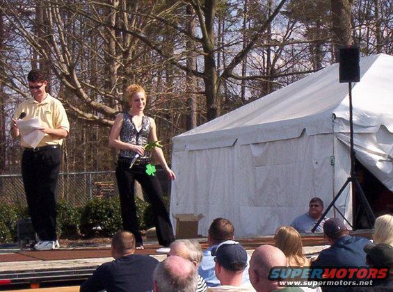 Man and woman on stage, tent in background, audience watching